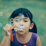 Adorable young girl enjoying summer outdoors while blowing bubbles, capturing pure childhood joy.