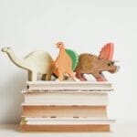 Colorful wooden dinosaurs on top of a stack of hardcover books on a light background.