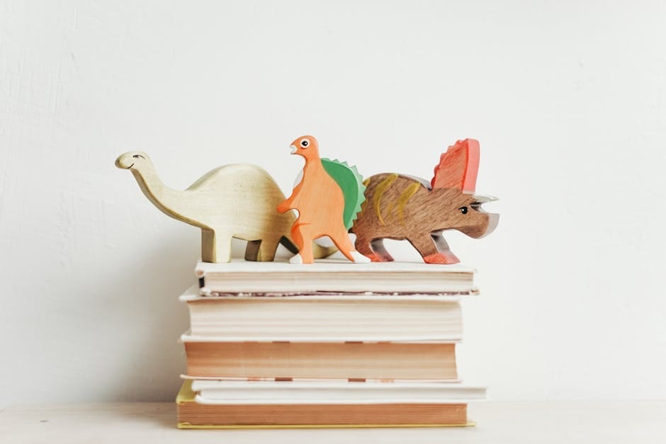 Colorful wooden dinosaurs on top of a stack of hardcover books on a light background.