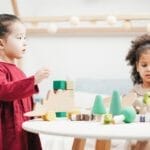 Two children engaging with wooden toys in a bright playroom. Ideal for education themes.