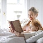 A mother and daughter enjoying a cozy moment reading together in a bright bedroom.