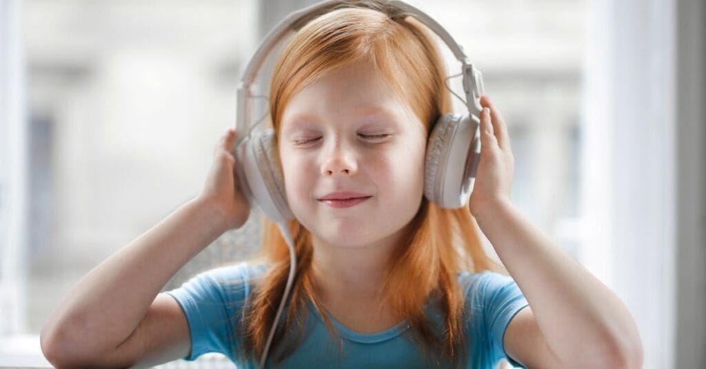 A young girl with headphones enjoying music indoors with a joyful expression.