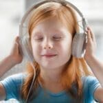 A young girl with headphones enjoying music indoors with a joyful expression.