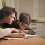 An attentive girl helps her younger brother concentrate on homework in a cozy home setting.