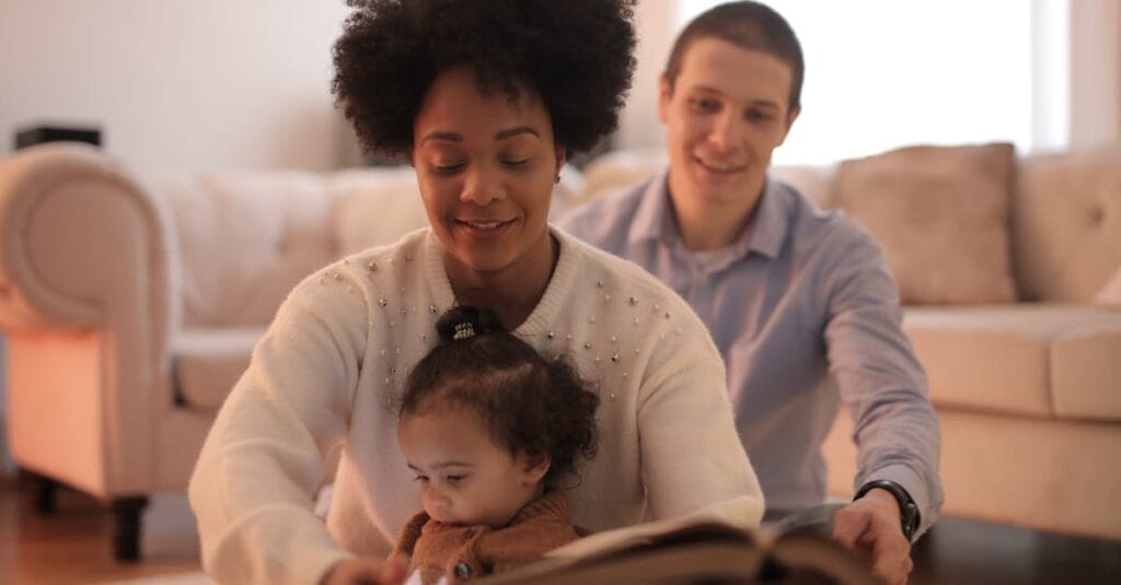 A family of three joyfully reading a book together in a warm, comfortable living room setting.