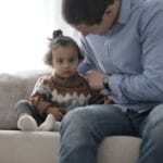 A father lovingly holds his child on a sofa, capturing a tender moment of parenthood indoors.