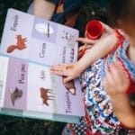 Young girl reading a colorful animal picture book outdoors, enjoying a sunny day in the park.