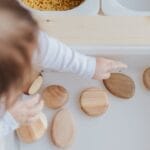 A toddler playing with wooden stones in a Montessori educational setup, promoting motor skills development.