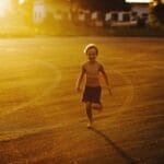 A happy child runs barefoot on a sunny day, enjoying the freedom of an open field at sunset.