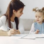 A mother and daughter enjoy quality time together coloring at a table indoors.