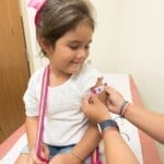 A cheerful young girl receives a band-aid after a vaccination at a clinic.