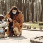 A mother and daughter wear masks and enjoy a walk with their dog in a park.