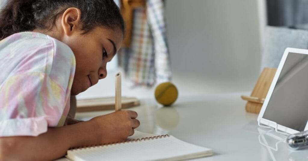 A young girl concentrating on homework at home using a tablet.