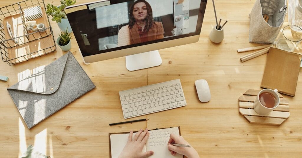 Person taking notes during a video call at a neatly organized home desk, showing remote work lifestyle.