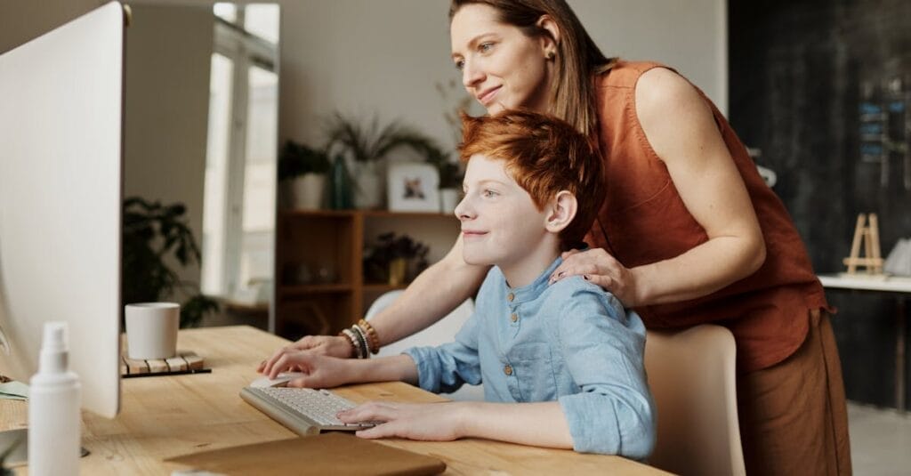 A mother and her child smiling while using a computer at home, focused on learning.