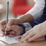 Close-up of hands guiding a child as they write in a notebook. Educational support scene.