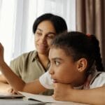 Mother and daughter engaged in online learning at home, using a laptop.