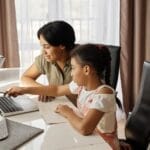 A mother assisting her daughter with online learning on a laptop, promoting education and family bonding.