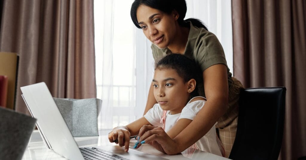 A mother helps her daughter with an online lesson on a laptop, showcasing family bonding and education at home.