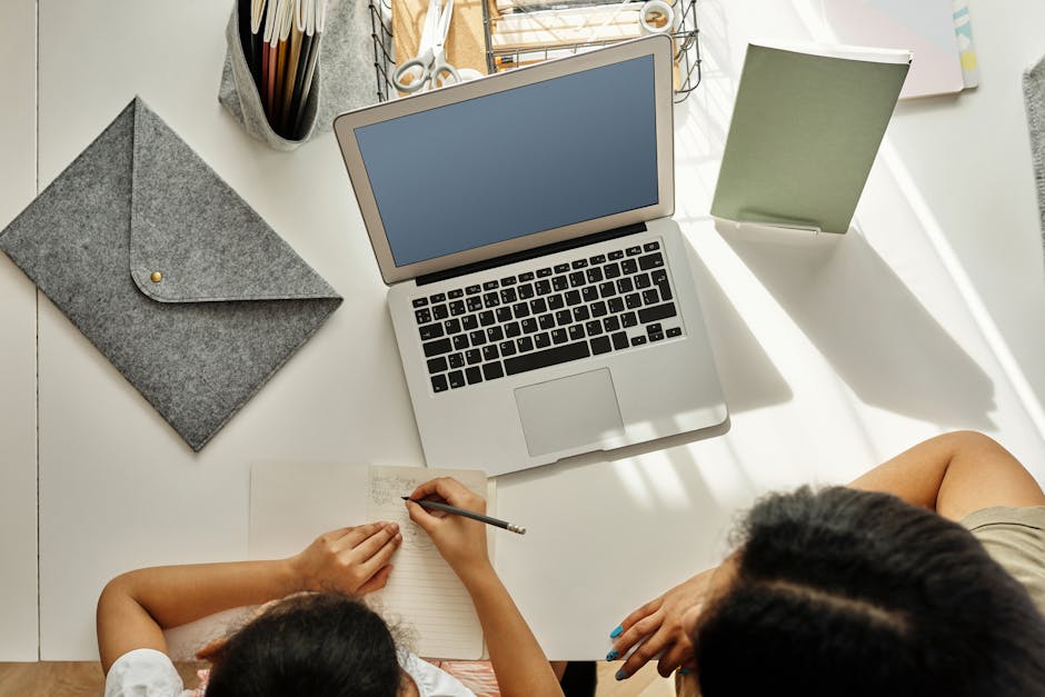 Mother helping daughter with homework at a desk with a laptop indoors.