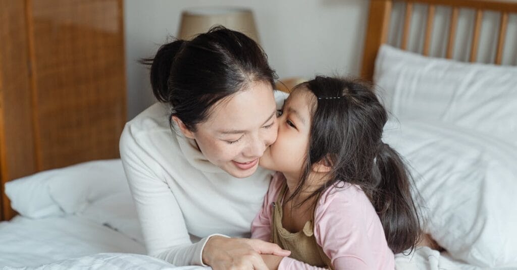 A loving mother and her daughter enjoy a cozy moment together on a bed, illustrating family bonding and affection.