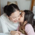 A loving mother and her daughter enjoy a cozy moment together on a bed, illustrating family bonding and affection.