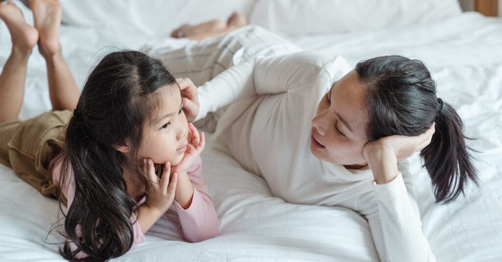 A mother and daughter bonding indoors, lying on a bed and enjoying quality time together.