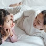 A mother and daughter bonding indoors, lying on a bed and enjoying quality time together.