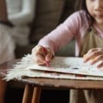 A child focuses on drawing while a parent works on a laptop in a cozy home environment.