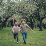 A cheerful father and two children running through a blossoming park, enjoying springtime together.