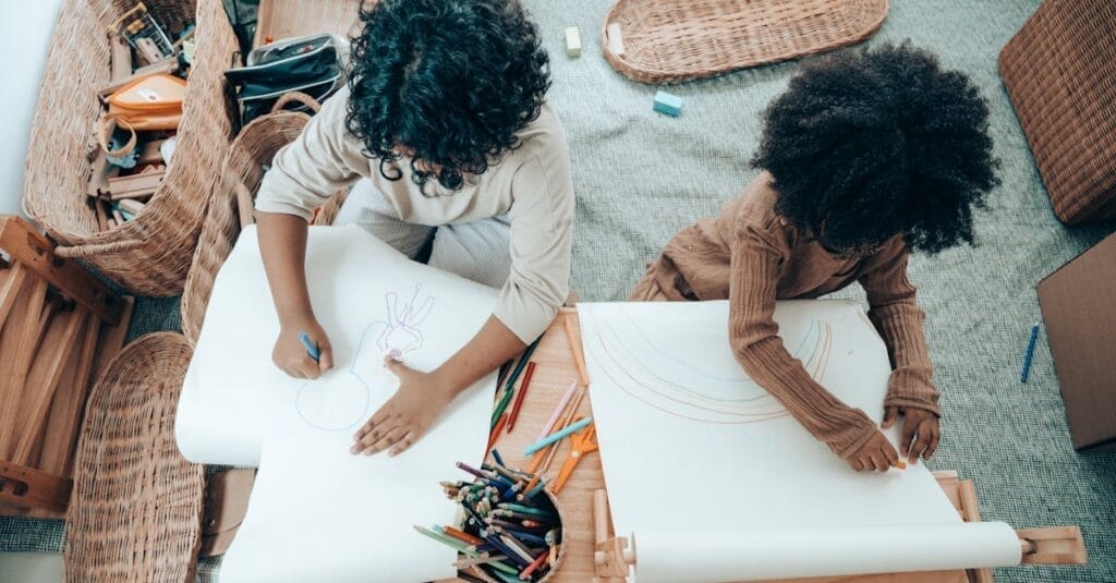 Two children drawing together at a desk filled with art supplies, fostering creativity in a cozy indoor setting.