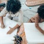 Two children drawing together at a desk filled with art supplies, fostering creativity in a cozy indoor setting.