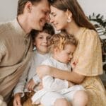 A loving family of four shares a tender moment in a cozy indoor setting, embracing and smiling.