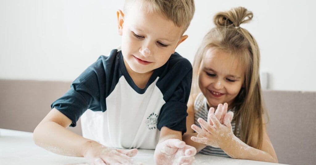 Two happy children enjoying baking, covered in flour while preparing dough at home.