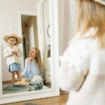 A mother and young daughter share a joyful moment dressing up indoors.