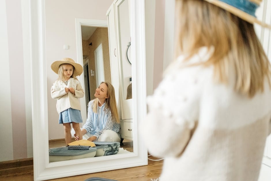 A mother and young daughter share a joyful moment dressing up indoors.