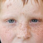 Close-up portrait of a freckled child's face with blue eyes captured outdoors, highlighting natural features.