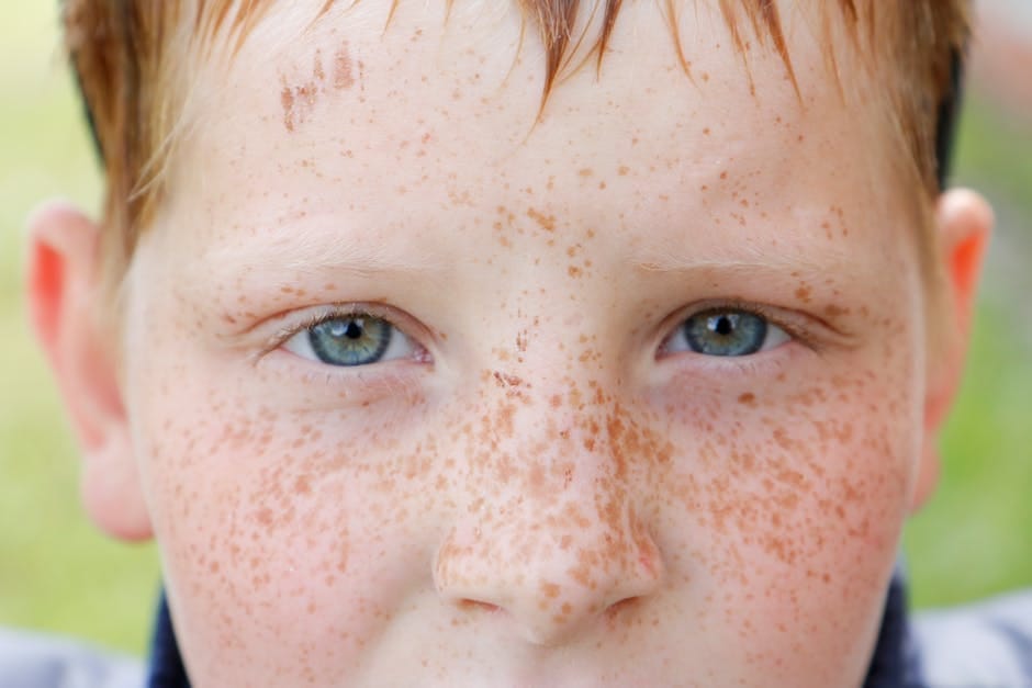 Close-up portrait of a freckled child's face with blue eyes captured outdoors, highlighting natural features.