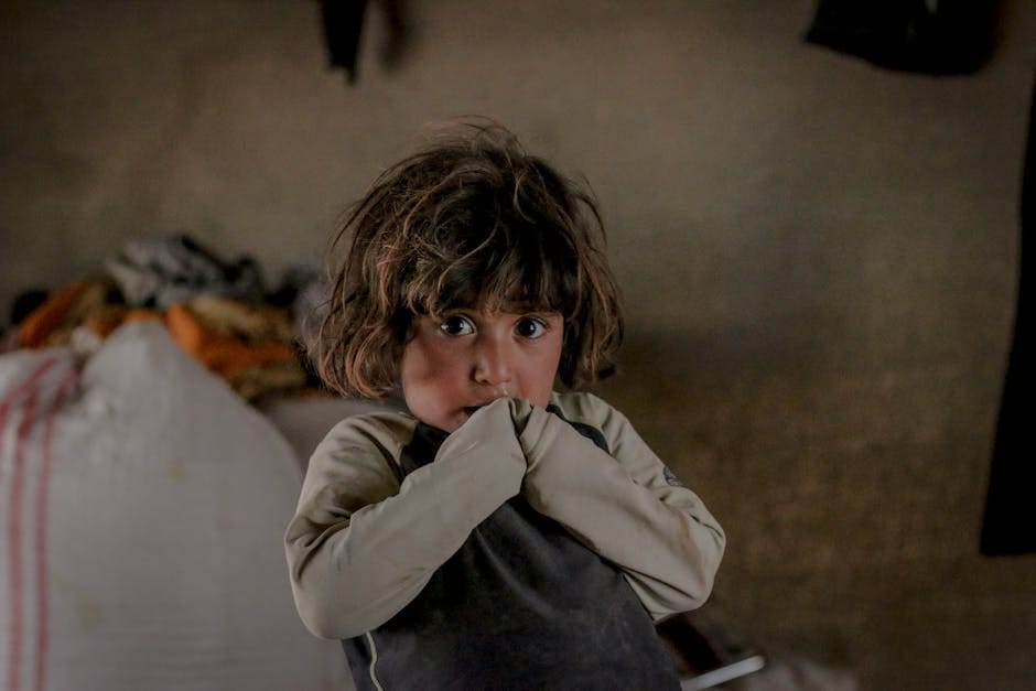 A child in a dimly lit room looking worried, with messy background.