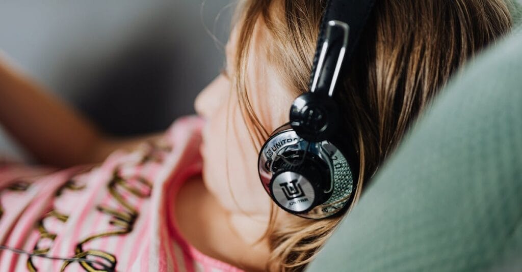 A young girl enjoys music using headphones while lounging comfortably indoors.