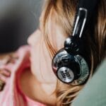 A young girl enjoys music using headphones while lounging comfortably indoors.