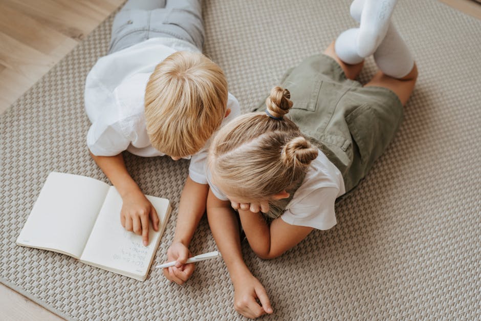 Two young children study together on the floor, concentrating on a notebook in a warm indoor setting.