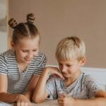 Two kids studying together at home, focusing on a book in a calm, indoor setting.