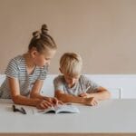 Two children studying together at home with books, emphasizing learning and concentration.