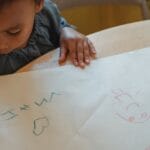 Child drawing with crayons on paper at home, expressing creativity and imagination.