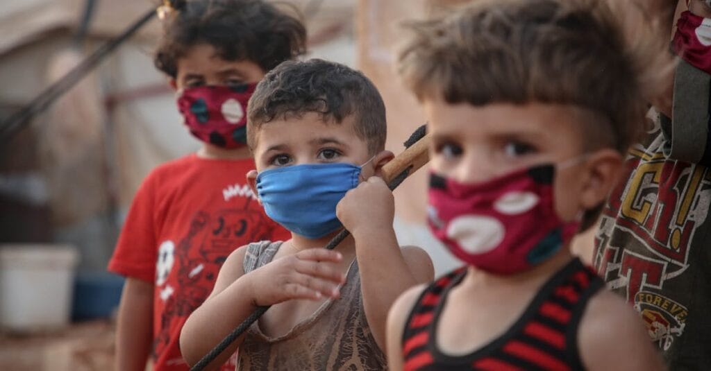 Young children wear face masks in a Syrian refugee camp, illustrating the impact of the pandemic.