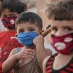 Young children wear face masks in a Syrian refugee camp, illustrating the impact of the pandemic.