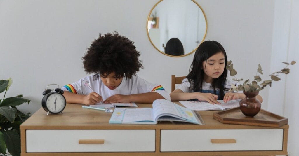 Concentrated multiracial girls sitting at table with notebooks and doing homework in cozy room
