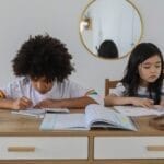 Concentrated multiracial girls sitting at table with notebooks and doing homework in cozy room