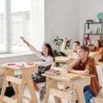 Students engage eagerly in a classroom, raising hands and participating in a lesson with their teacher.